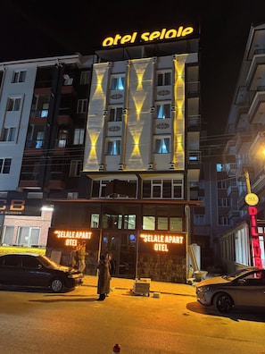 Ein Hotel mit einer gut sichtbaren, beleuchteten Schautafel, einem Eingangsbereich auf Straßenniveau und einem Parkplatz.