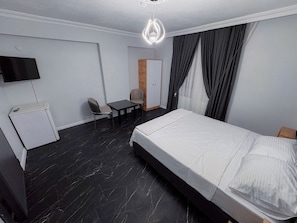 A hotel room with a bed, a desk, a chair, a wardrobe, and a television.