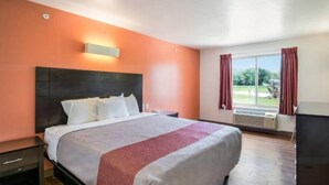 Habitación de hotel con cama, mesita de noche, escritorio y ventana con cortinas.