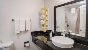 Un baño con lavamanos blanco, espejo y toallero.