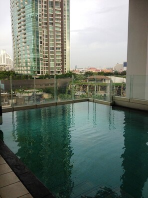 A rooftop swimming pool with a glass barrier, surrounded by high-rise buildings and a view of the cityscape. - Luxurious 2-Bedroom Apartment Near Chao Phraya River (Bangkok)