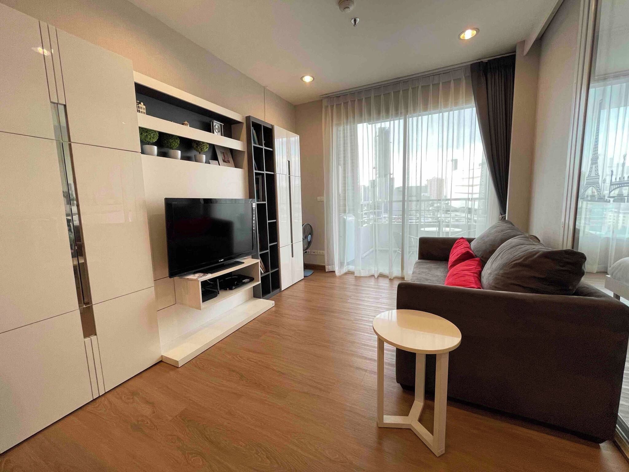 A modern living room with a flat-screen TV, built-in shelving, a sofa, and a small table.
