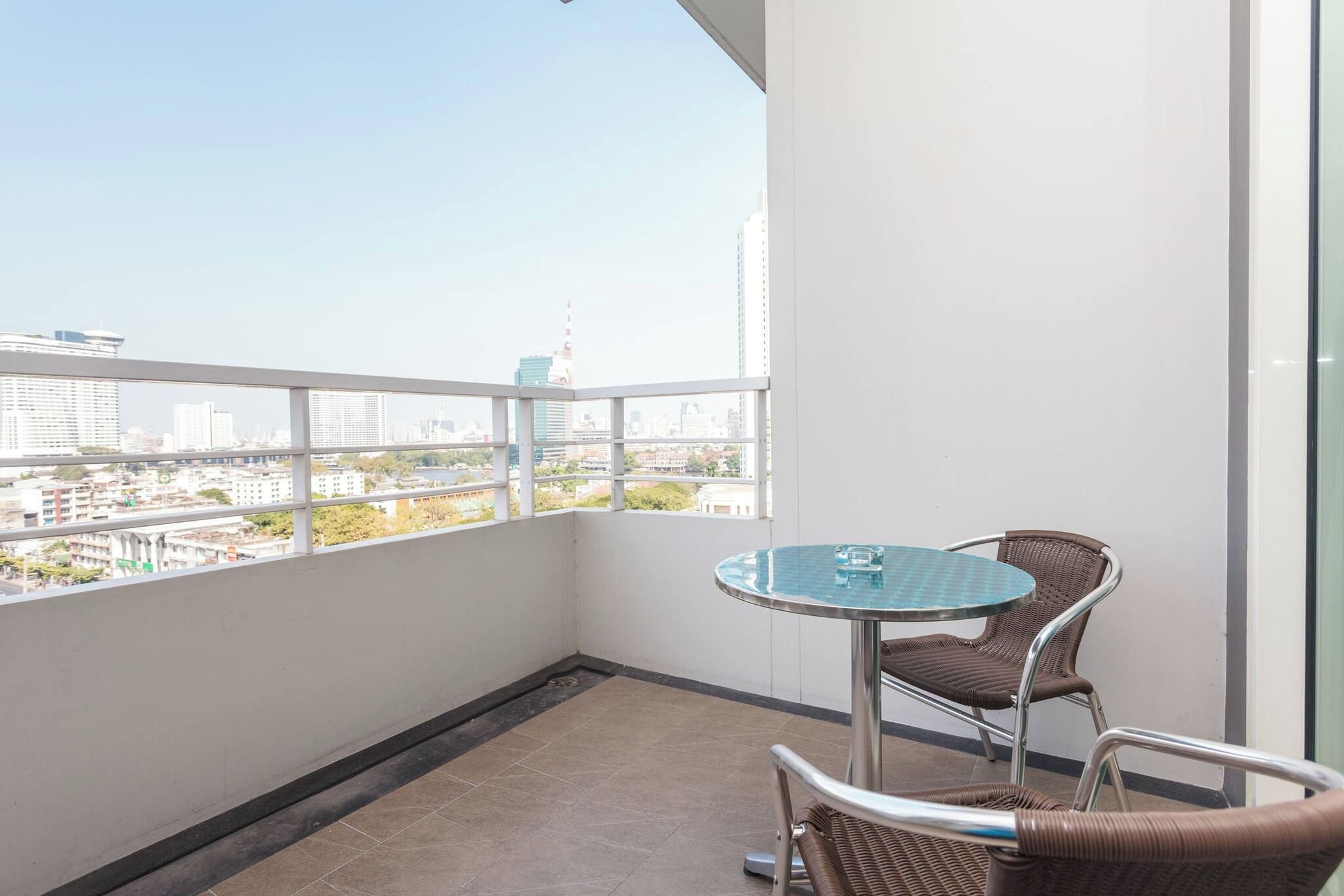 Ein Balkon mit Glastisch und Korbstühlen, der auf einen Stadtblick mit Gebäuden und einem Fluss ausgerichtet ist.