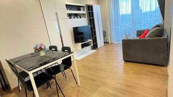 A modern living space with a dining area, a sofa, a TV, and a window with curtains.