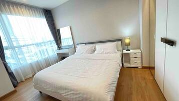 A modern hotel room with a large bed, a bedside table with a lamp, and a view of the city through the window.