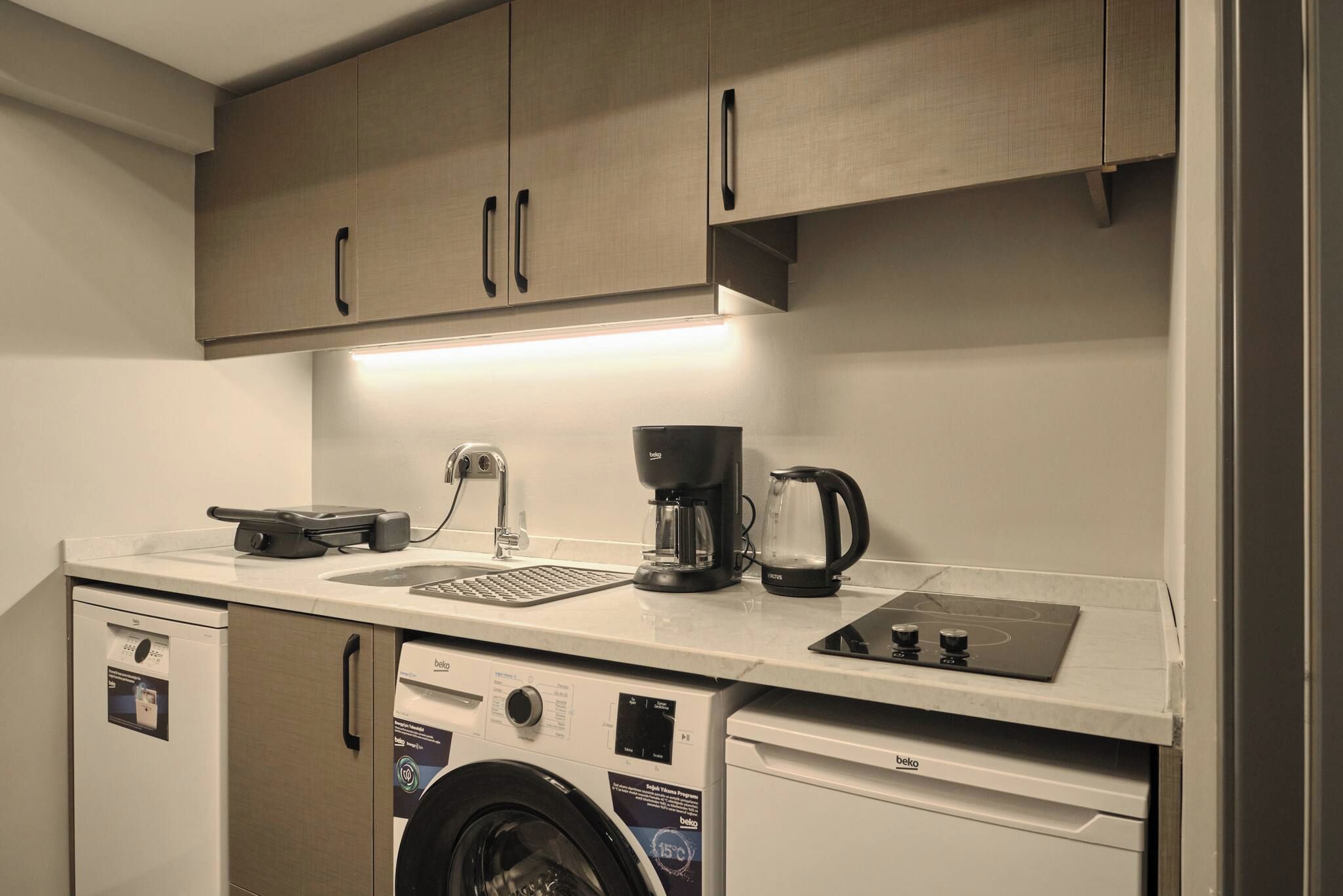 A compact kitchenette with a washing machine, a coffee maker, and a small sink.