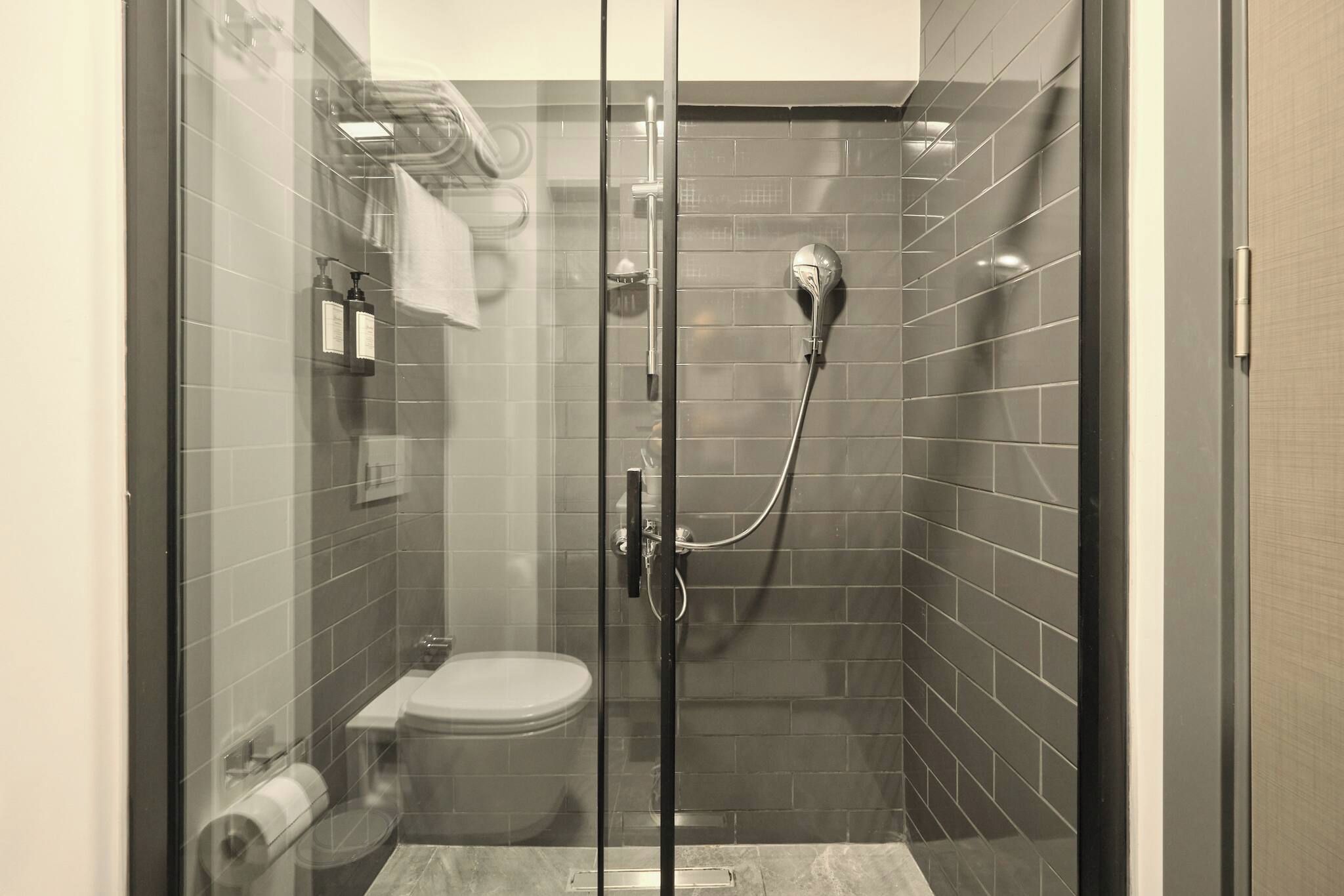 A glass-enclosed shower stall with a toilet and a towel rack.