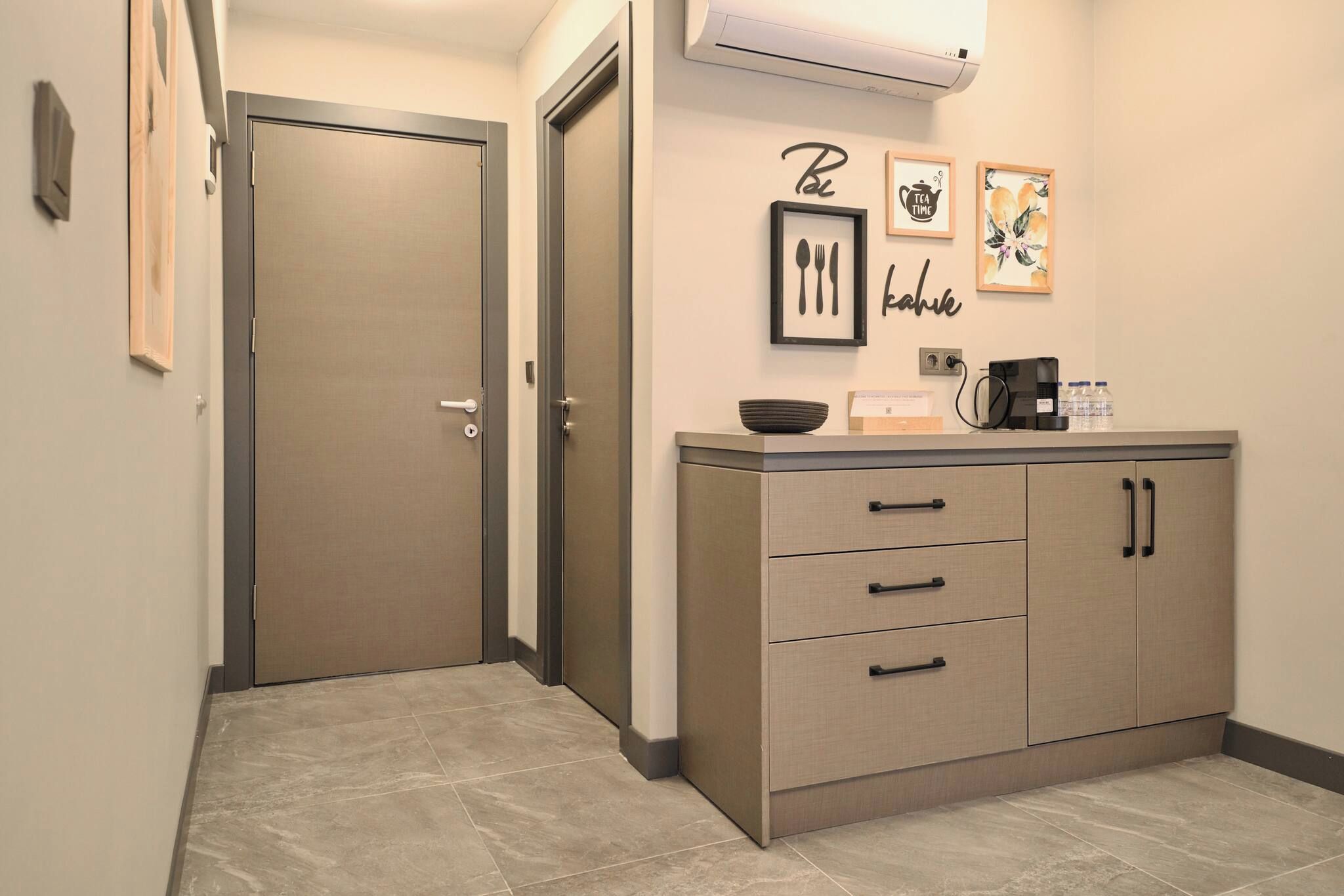 A hallway with a door, a kitchenette with a coffee maker, and wall art.