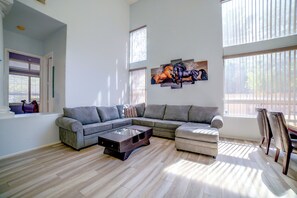 A modern living room with a sectional sofa, a glass coffee table, and a large window with blinds.