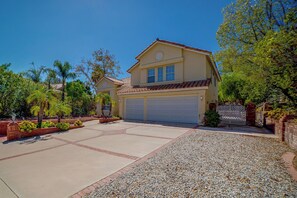 A two-story house with a garage, surrounded by a landscaped garden with palm trees and shrubs.