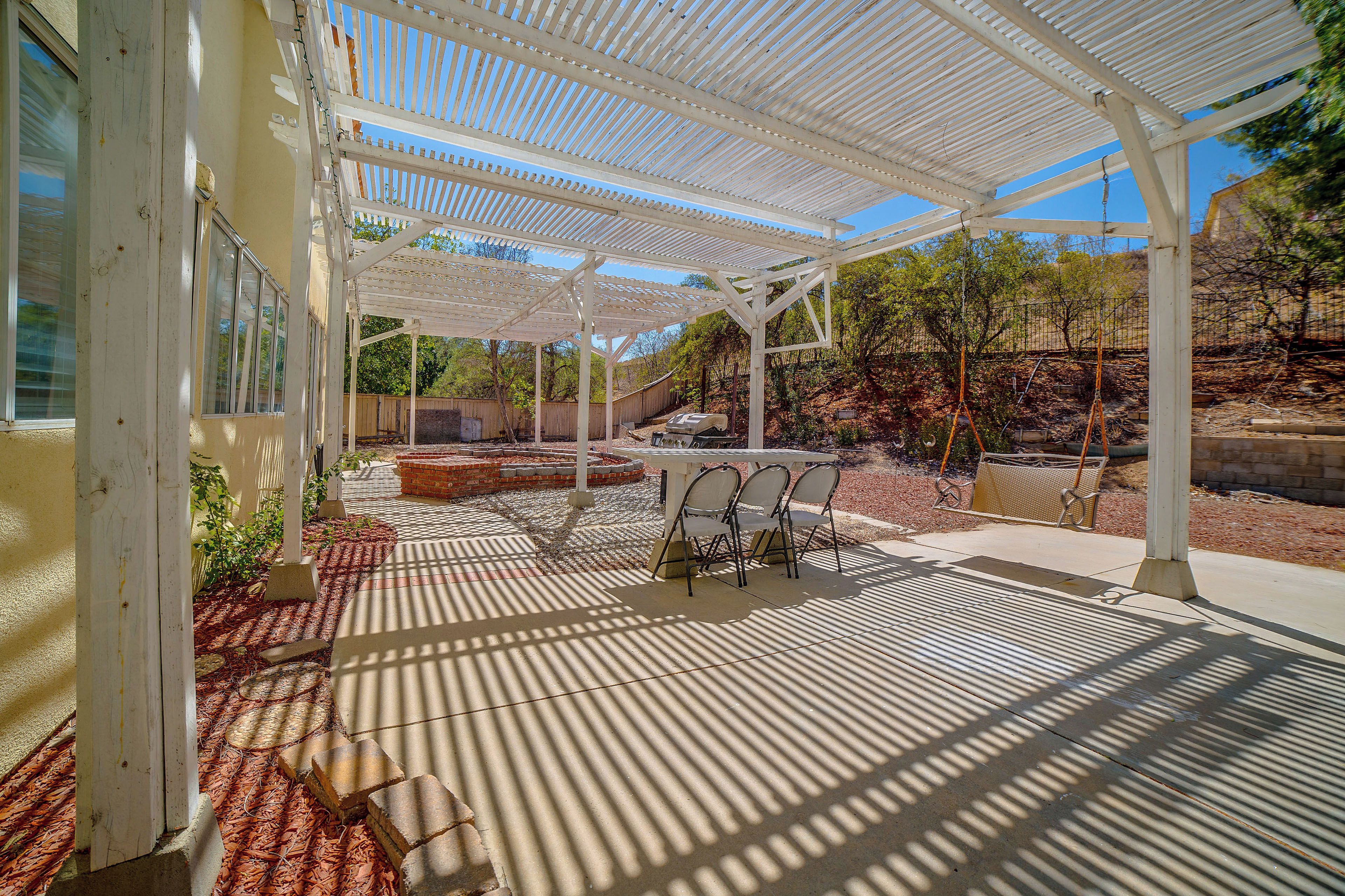 A covered patio area with a pergola, outdoor seating, and a barbecue grill.