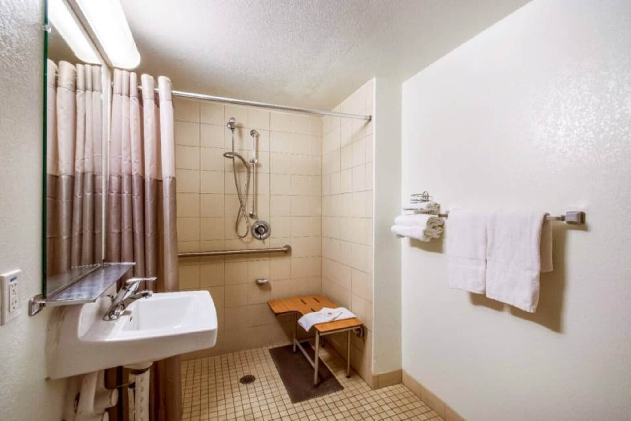 Un baño pequeño con lavamanos, espejo, ducha y toallero.