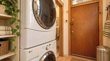 A laundry area with stacked washers and dryers, a wooden door, and a shelf with towels and baskets.