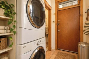 A laundry area with stacked washers and dryers, a wooden door, and a shelf with towels and baskets.