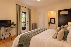 A bedroom with a bed, a desk, a television, and a door.
