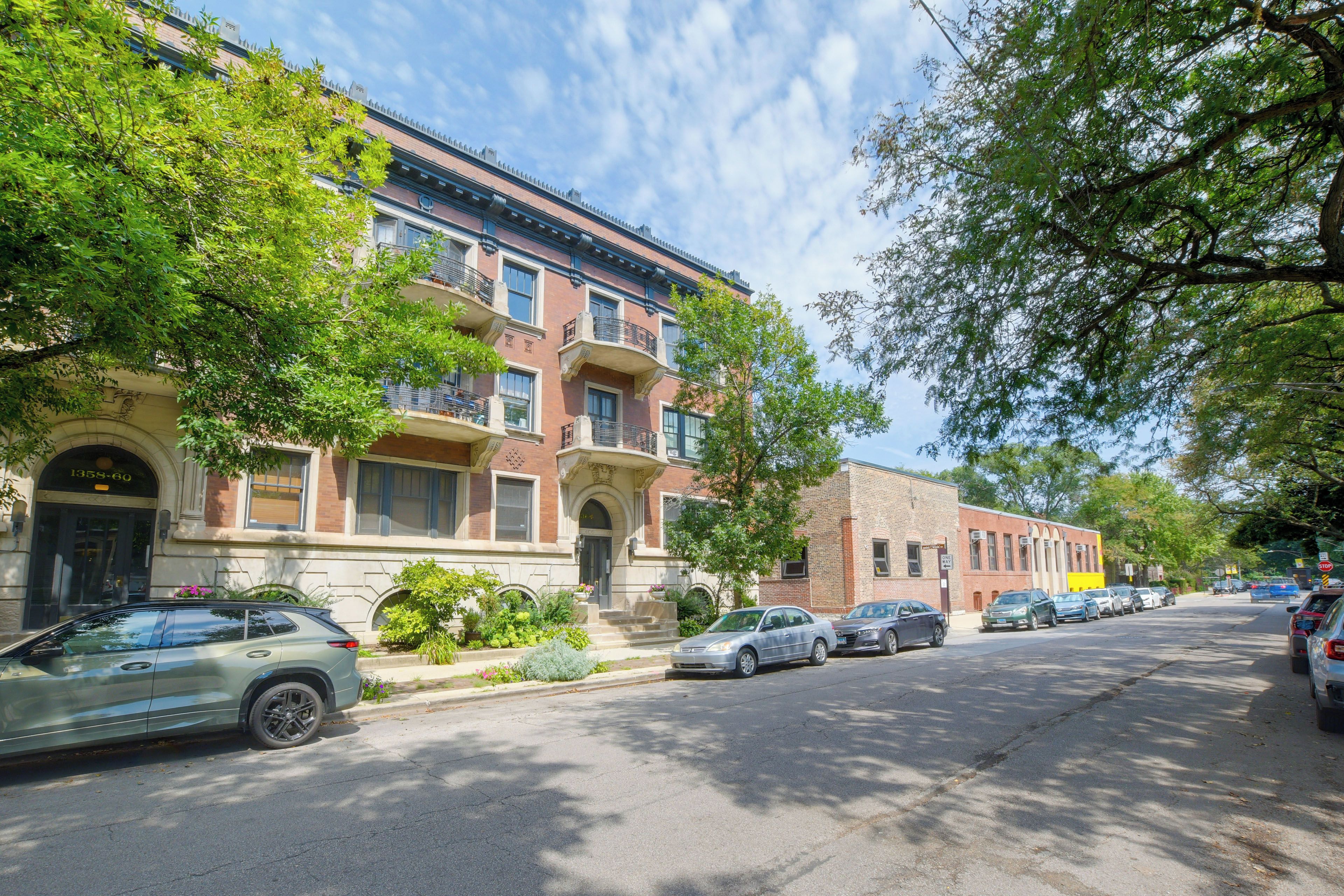 A row of brick townhouses with a central courtyard, parked cars, and mature trees.