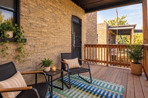 A covered outdoor seating area with brick walls, a wooden deck, and potted plants.