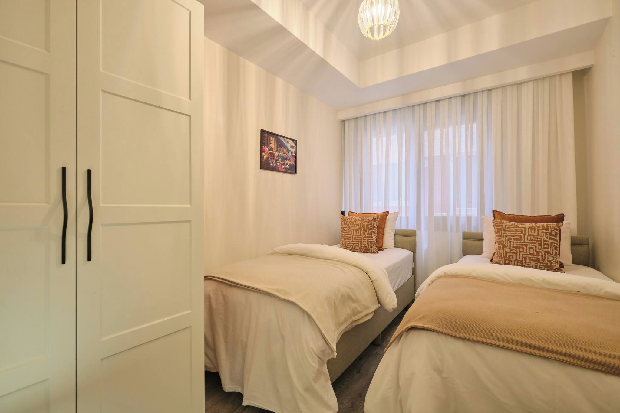 Een hotelkamer met twee bedden, een kledingkast, een schilderij aan de muur en een raam met gordijnen.