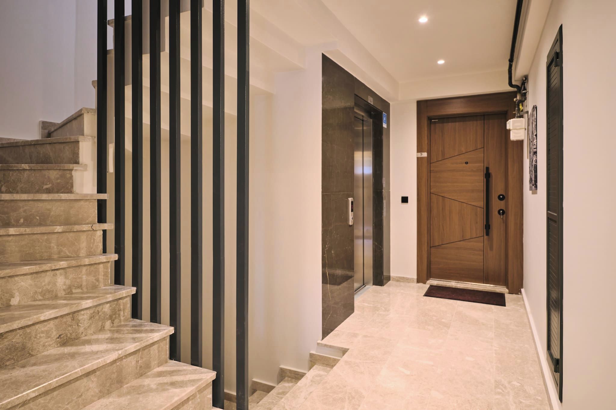 Ein modernes Interieur mit einer Marmortreppe, einem gläsernen Aufzug und einer Holztür.