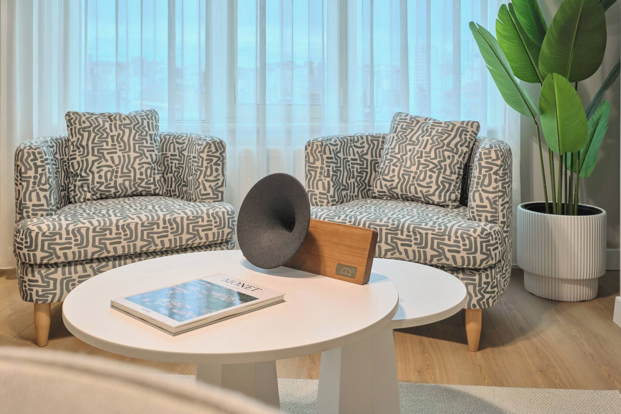 A modern living room with patterned sofas, a round coffee table, and a potted plant.