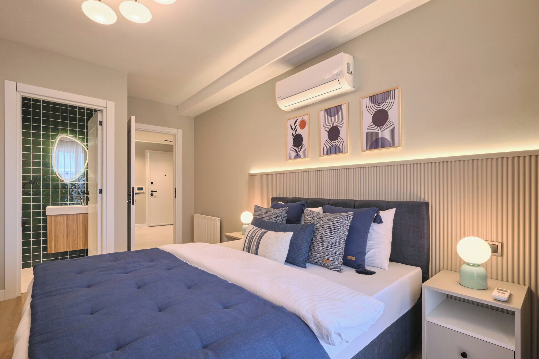 A modern bedroom with a large bed, bedside tables, an air conditioning unit, and decorative wall art.