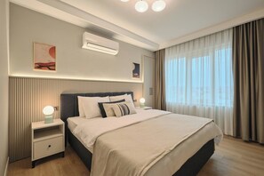 Una habitación de hotel moderna con una cama grande, lámparas de noche, un equipo de aire acondicionado y una ventana con cortinas.
