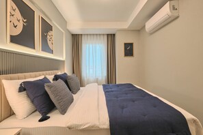 A hotel room with a bed, a headboard, a window with curtains, and wall-mounted air conditioning. - Spassky, 3BR, Minimalist, Well-equipped (Kadıköy)