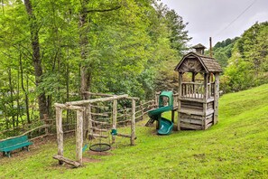 Eine Holzspielgeräte-Konstruktion mit Rutsche und Schaukeln, umgeben von üppigem Grün.