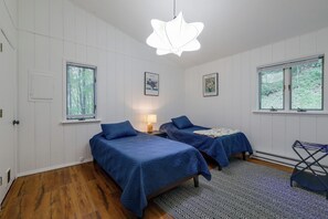 Ein Zimmer mit zwei Betten, einem Fenster, einer Tür und einer Hängeleuchte.