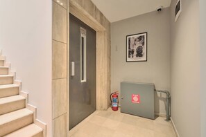 Un passadís amb una escala, una porta, un extintor i un quadre al mur.