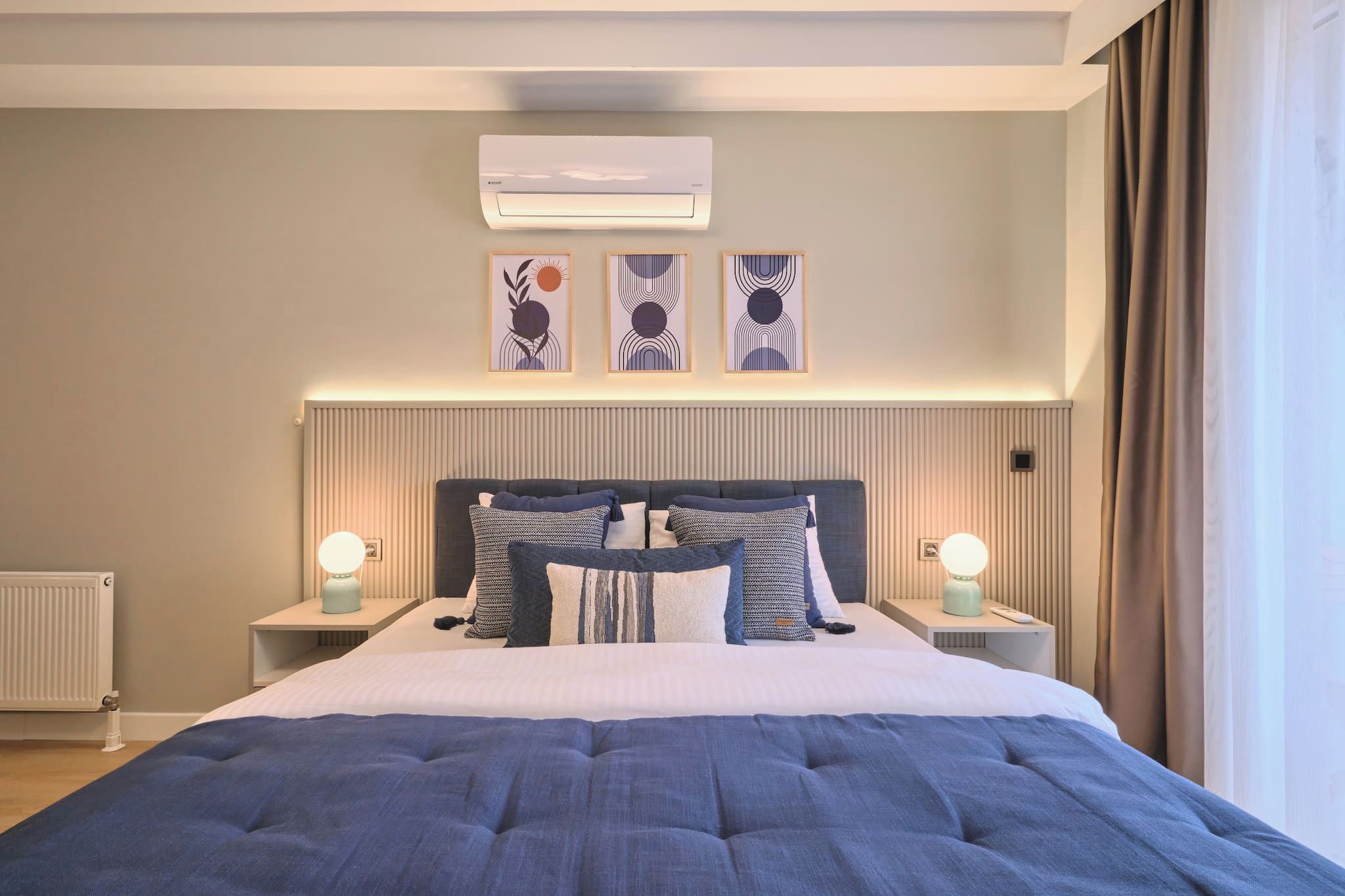 Een hotelkamer met een groot bed, twee nachtkastjes met lampen, een radiator en een wandairconditioner.