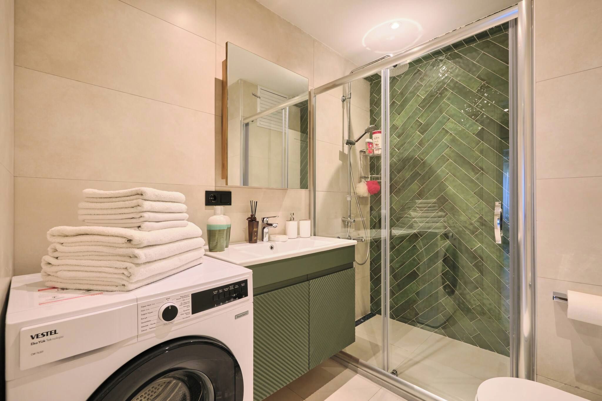 Un baño moderno con lavadora, lavamanos y cabina de ducha de vidrio.