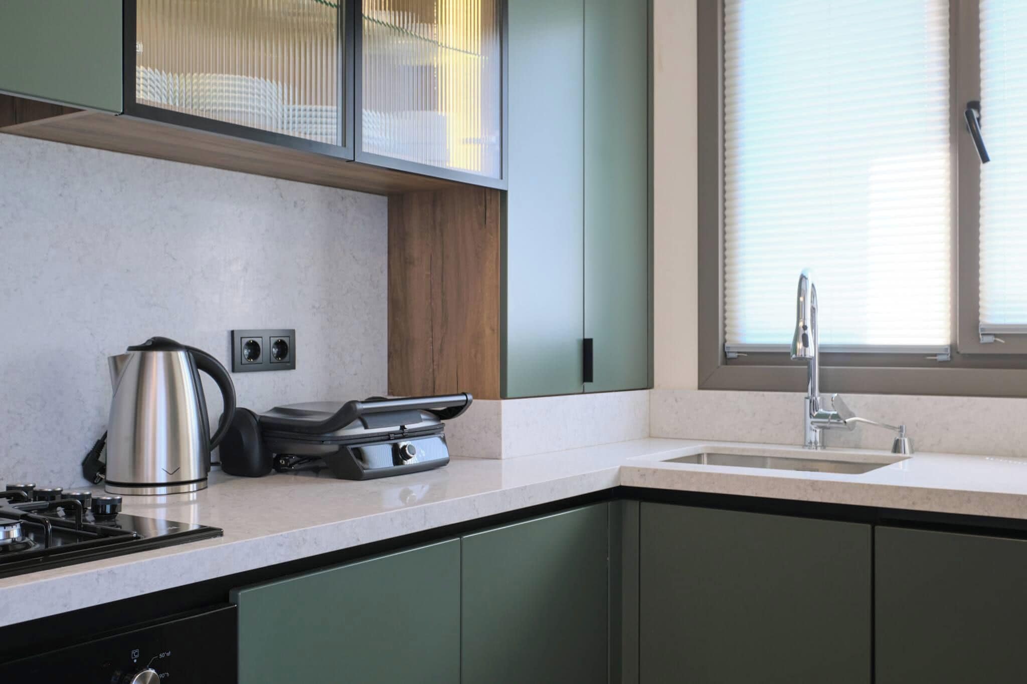A modern kitchen with a gas stove, a kettle, a toaster, and a sink with a faucet.