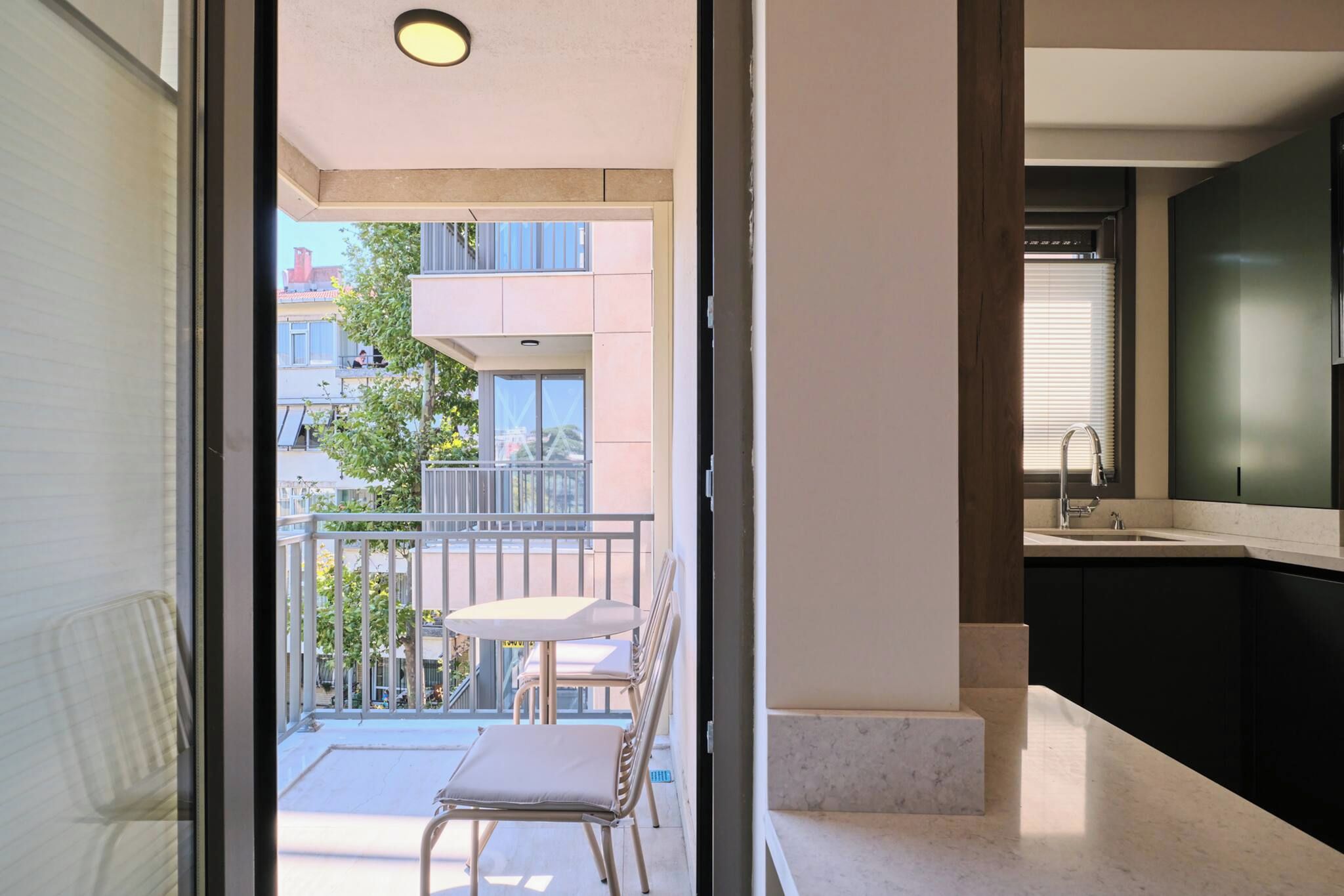 An interior view of a modern apartment with a balcony, a dining area, and a kitchen.