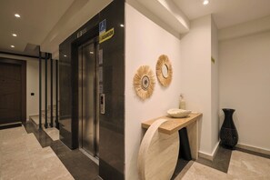 Un ascensor modern amb un pantalla digital, un mirall decoratiu penjat a la paret i una taula petita amb un vas.