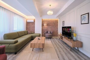 A modern living room with a sofa, coffee table, and a TV on a wooden stand. - Orion, Fancy 2BR, Best Loc (Kadıköy)