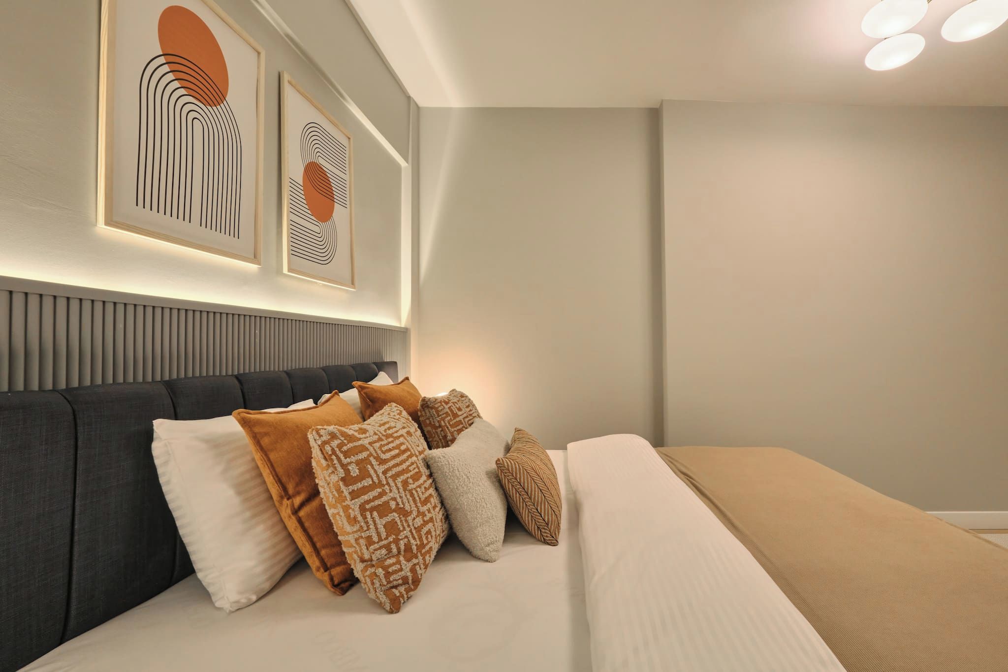 A modern bedroom with a large bed, multiple pillows, a headboard, and framed artwork on the wall.