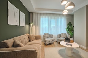 A modern living room with a sectional sofa, two patterned armchairs, a coffee table, and a large plant. - Fischer, 2BR, Bright, Stylish (Kadıköy)
