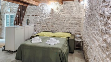 A room with a bed, a desk, and a stone wall.