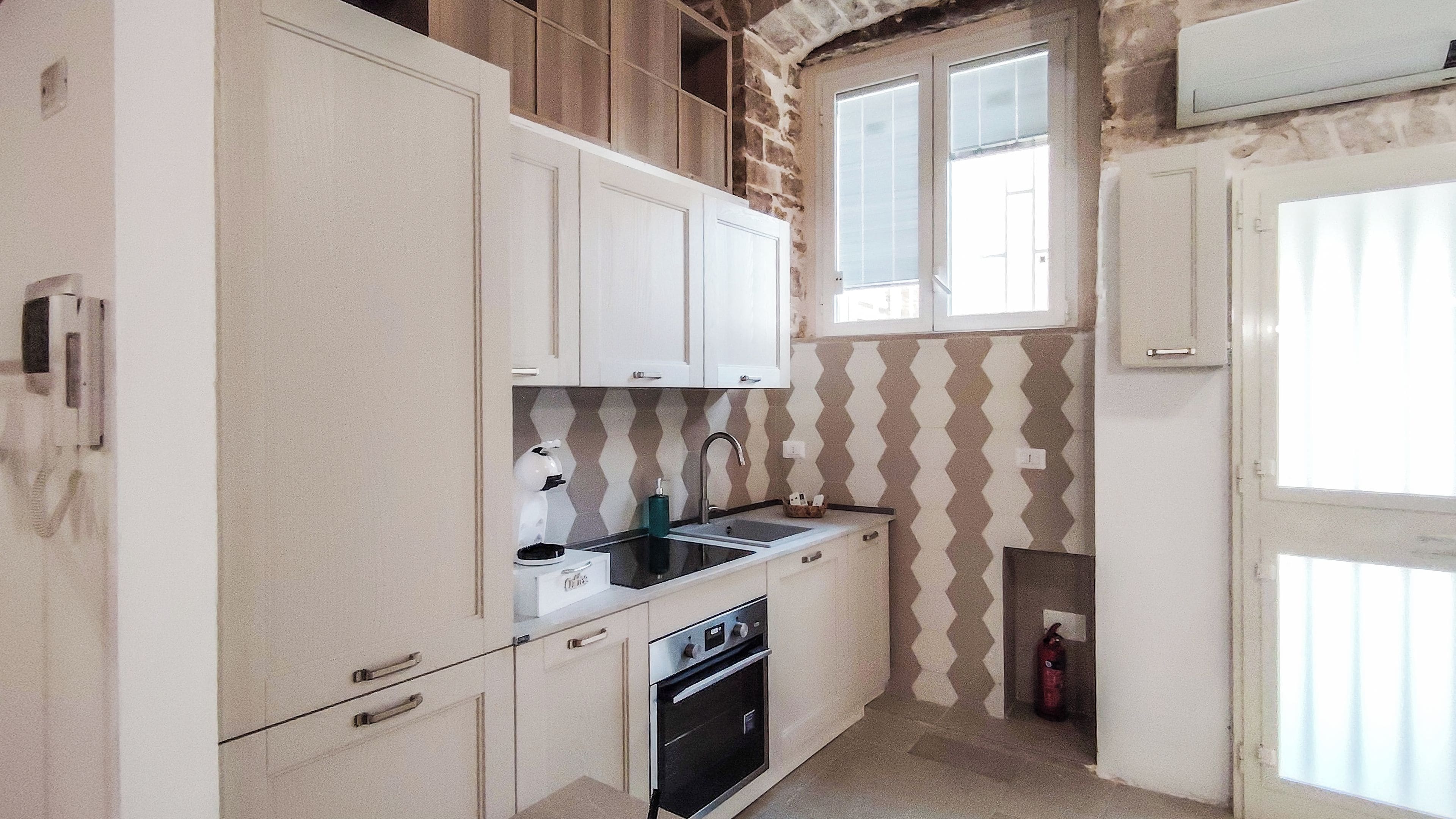 Een kleine keuken met witte kasten, een zwarte spoelbak en een inbouwoven.