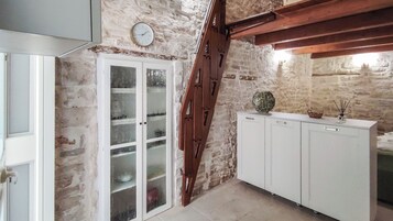 Una habitación con pared de piedra, escalera de madera, un armario blanco y una puerta con paneles de vidrio esmerilado.