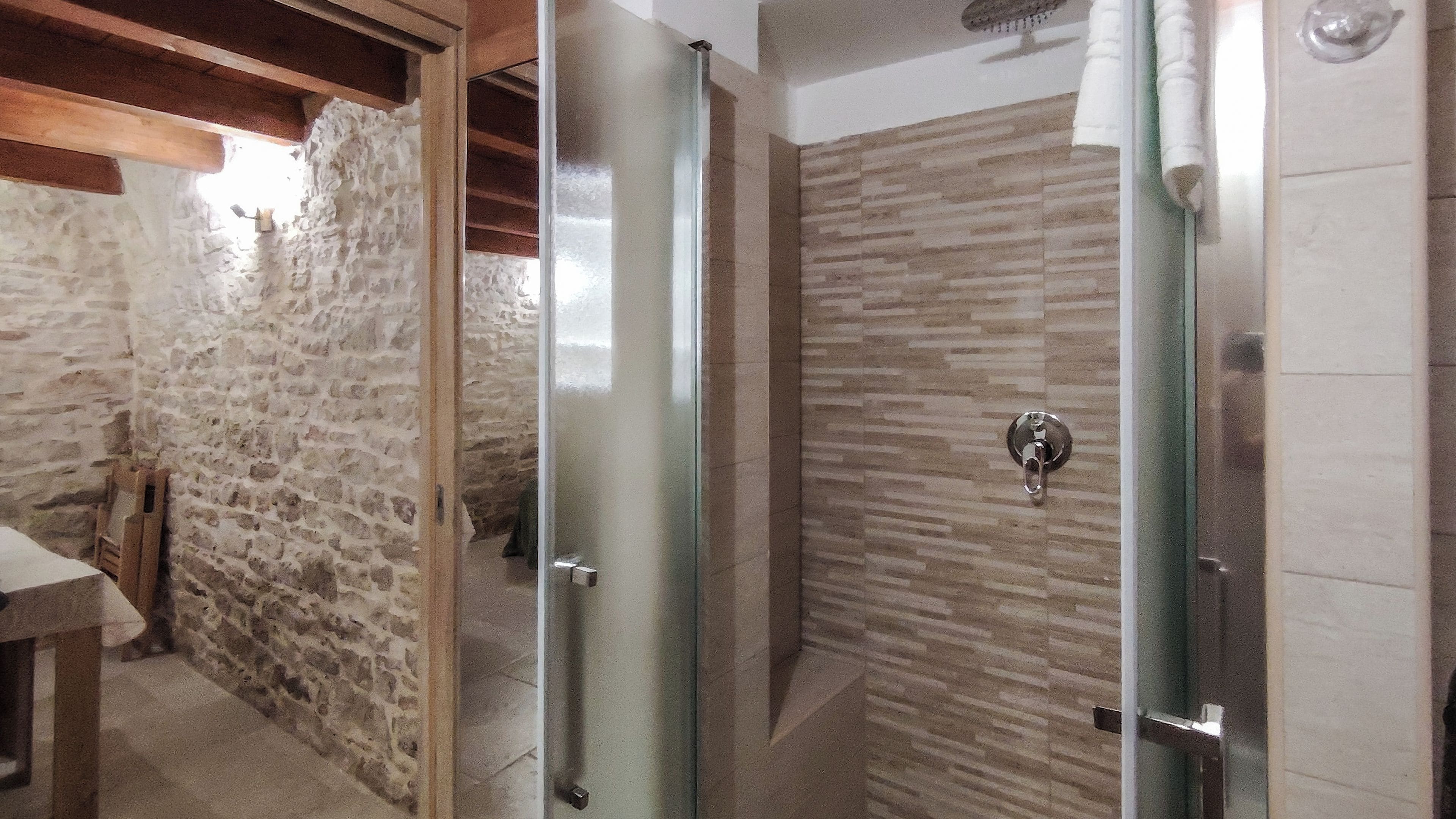 Une salle de bain aux murs en pierre, avec un plafond orné de poutres en bois et un sol carrelé.