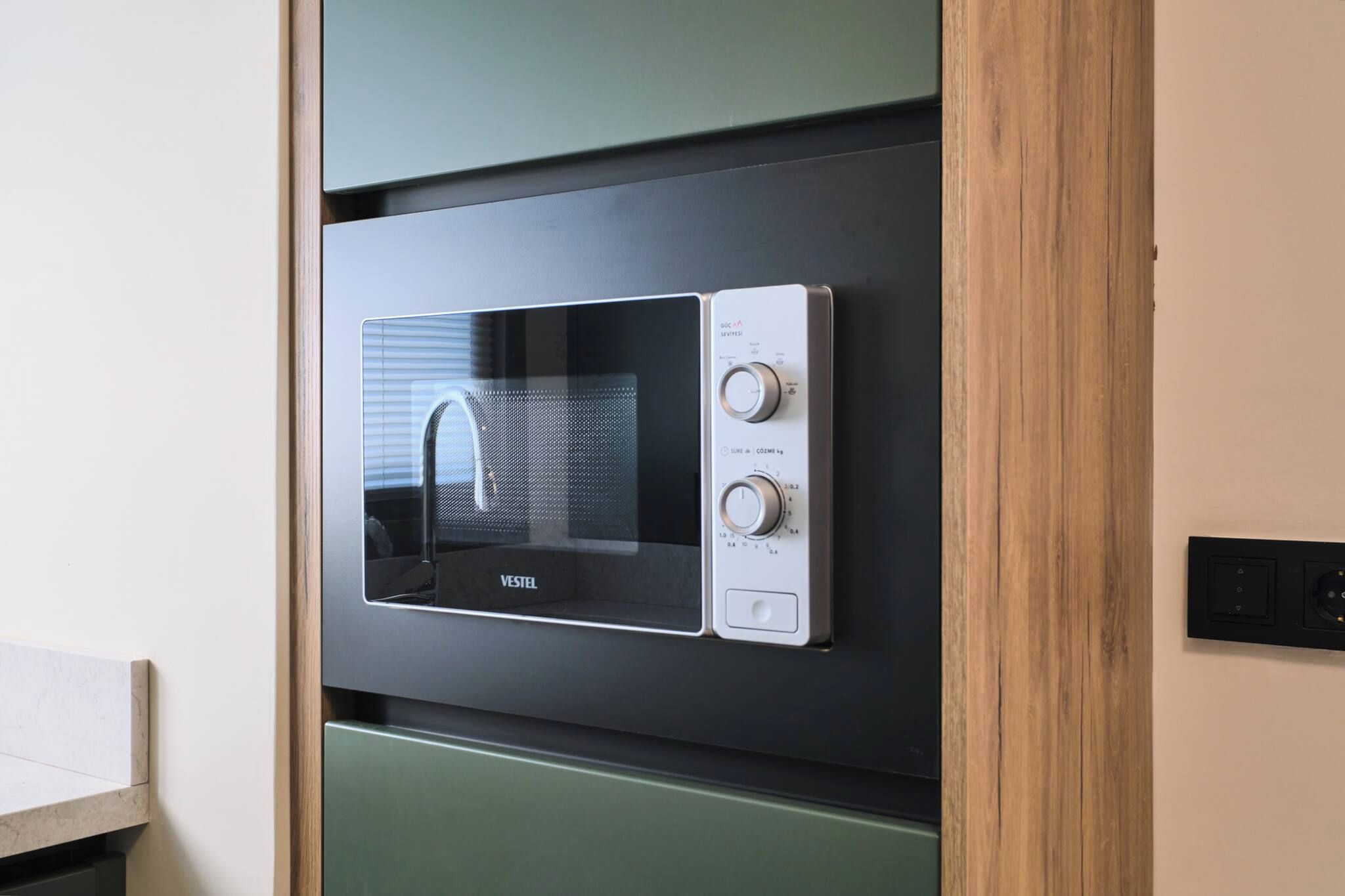 A microwave oven with a digital display and control knobs, mounted on a wall with a wooden frame.
