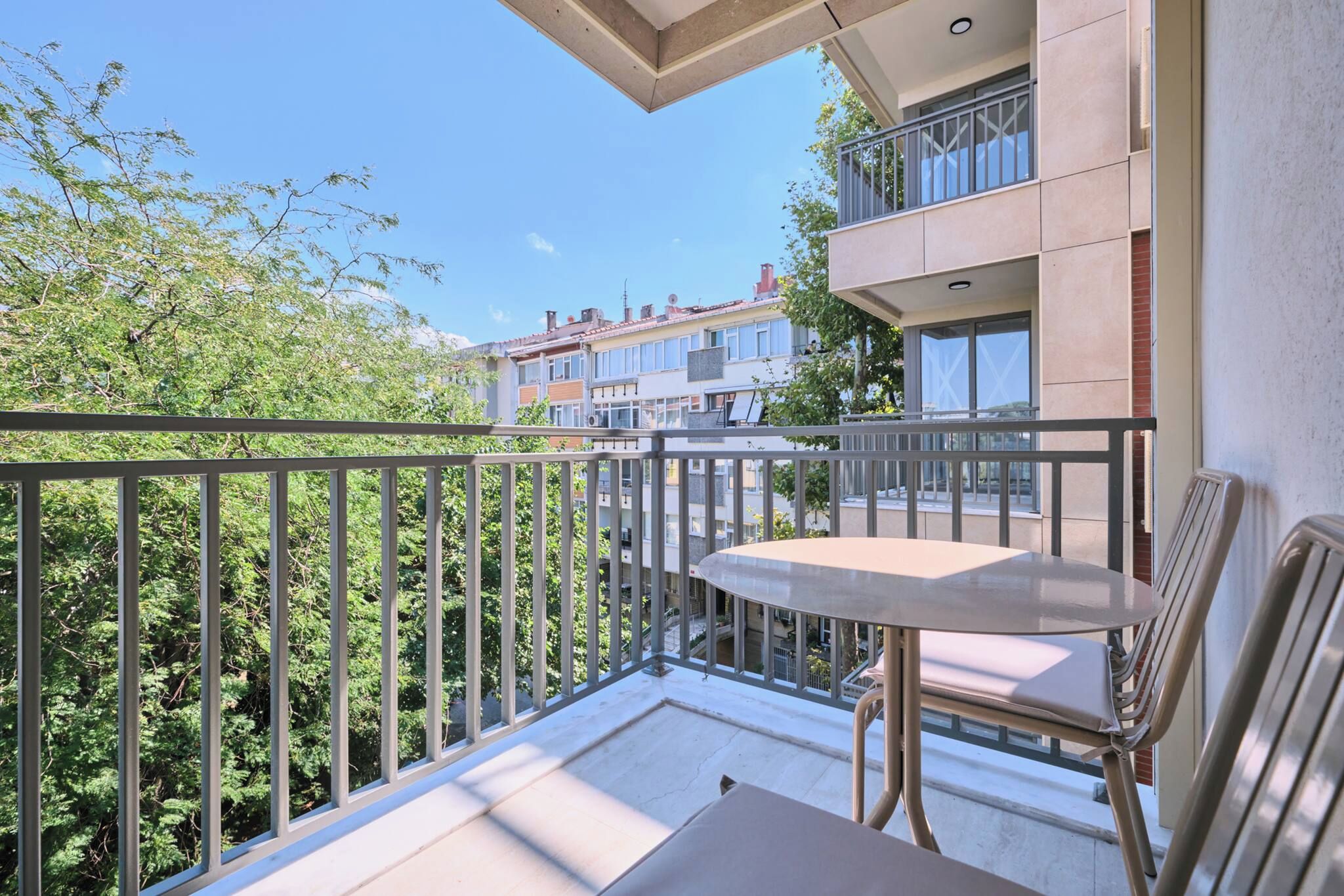 Ein Balkon mit Tisch und Stühlen, mit Blick auf eine Wohngegend mit Bäumen und Gebäuden.