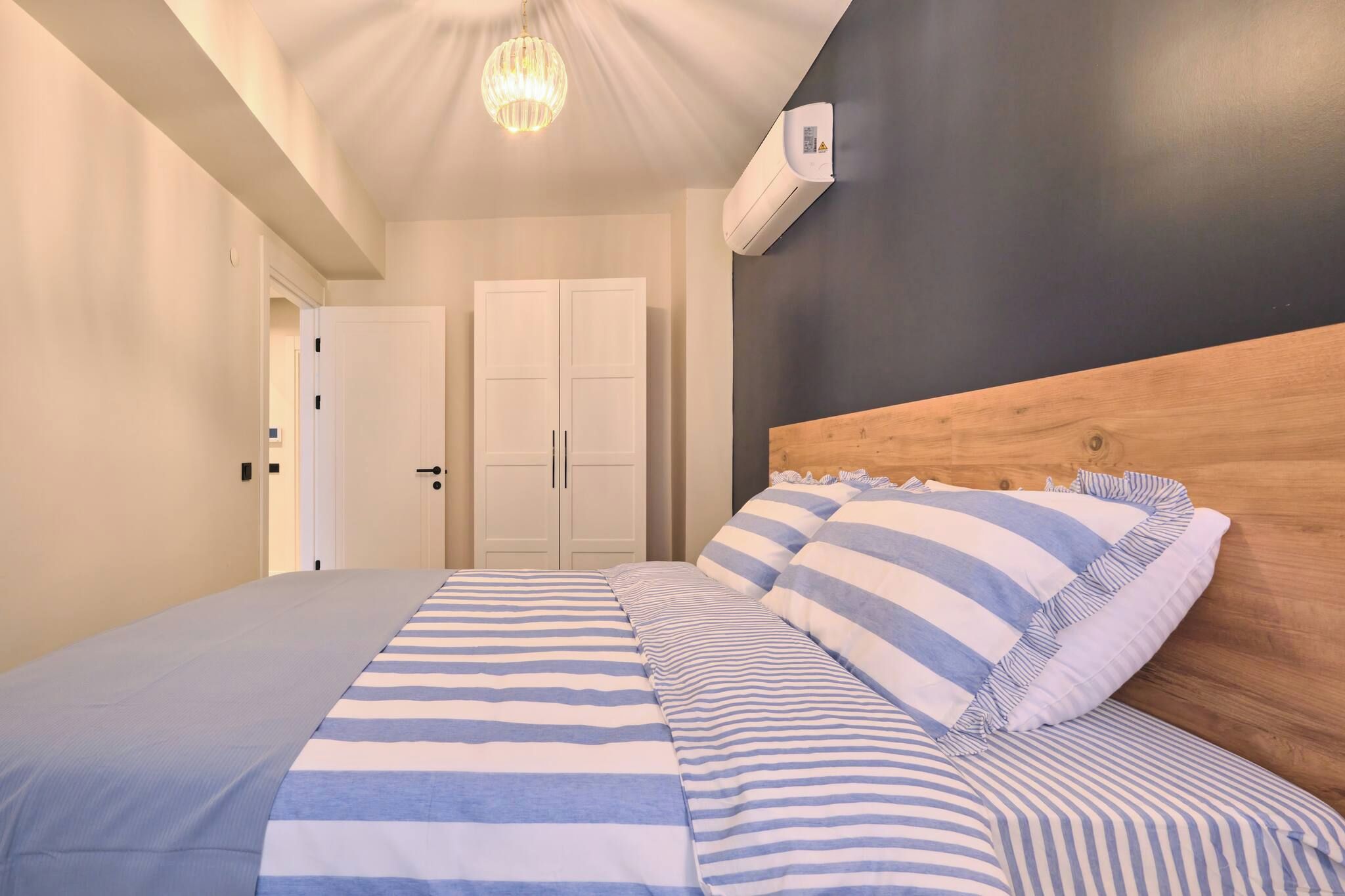 A bedroom with a bed, a wooden headboard, a ceiling light, and a wall-mounted air conditioning unit.