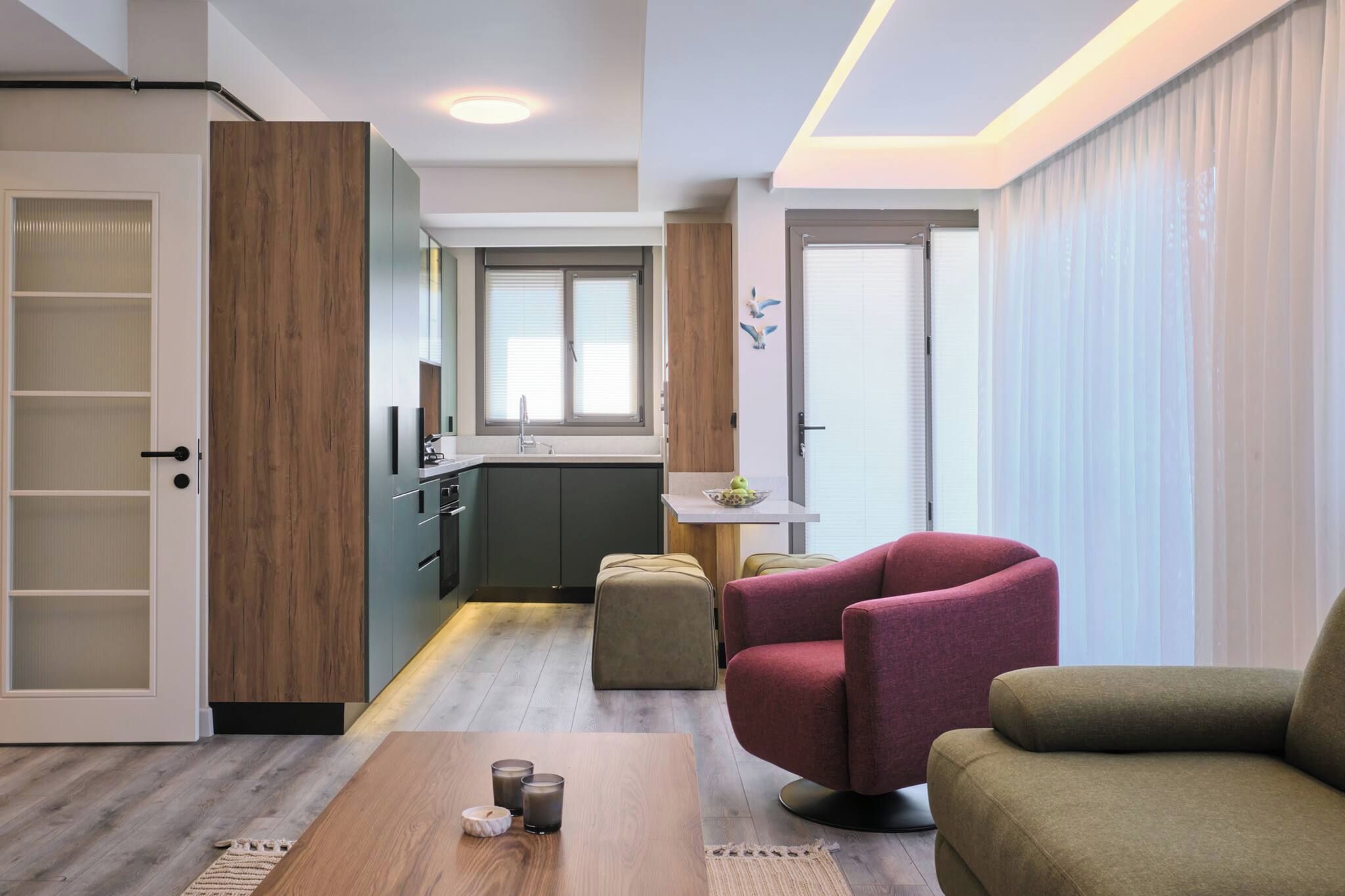 Een moderne woonkamer met een houten salontafel, twee fauteuils, een keukenhoek met raam en een schuifdeur.