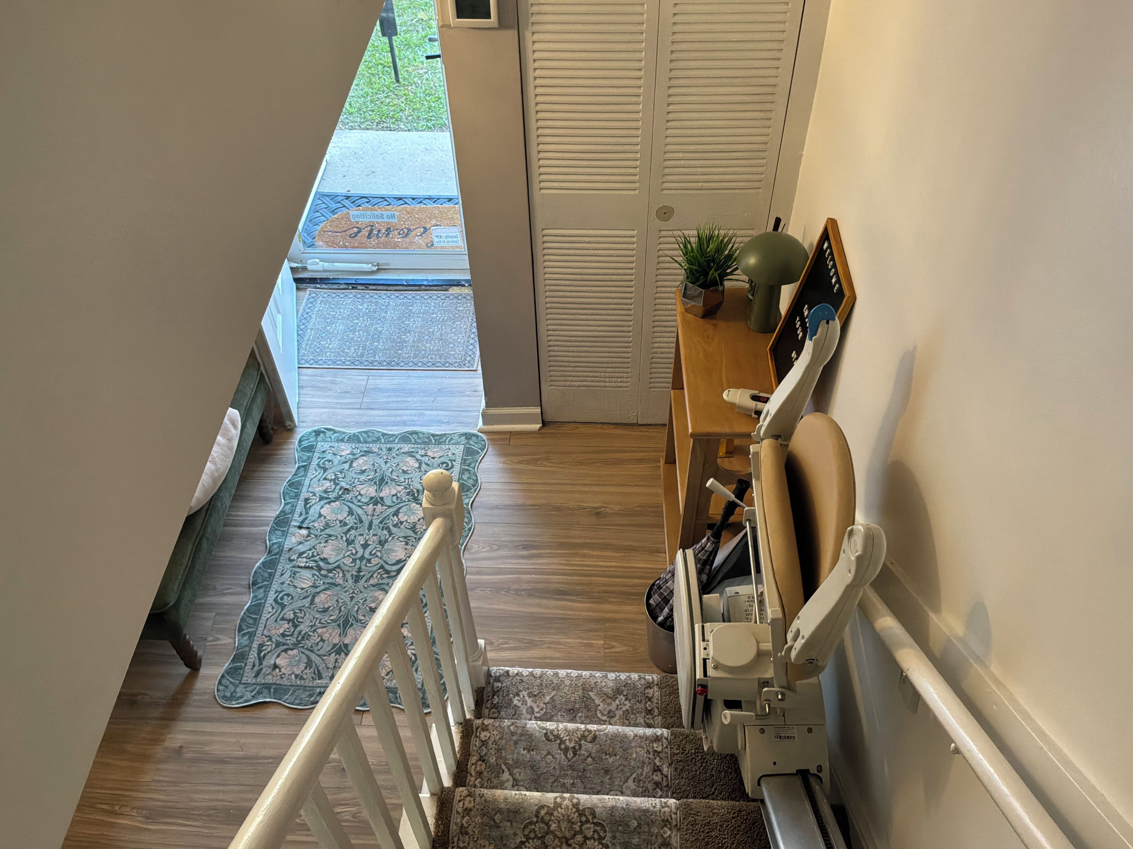 A staircase with a handrail, a wooden floor, a patterned rug, and a door with louvered panels.