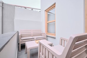 En liten, avskärmad balkong med en vit soffa, ett litet bord och en trästol.