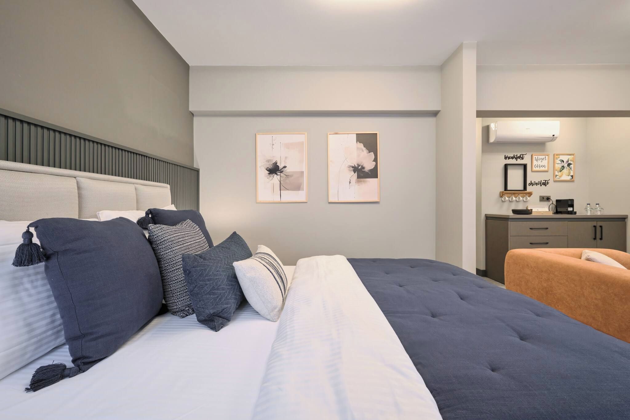Un dormitori modern amb un llit gran, una taula de nit, un petit sofà i una zona de cuina compacta.
