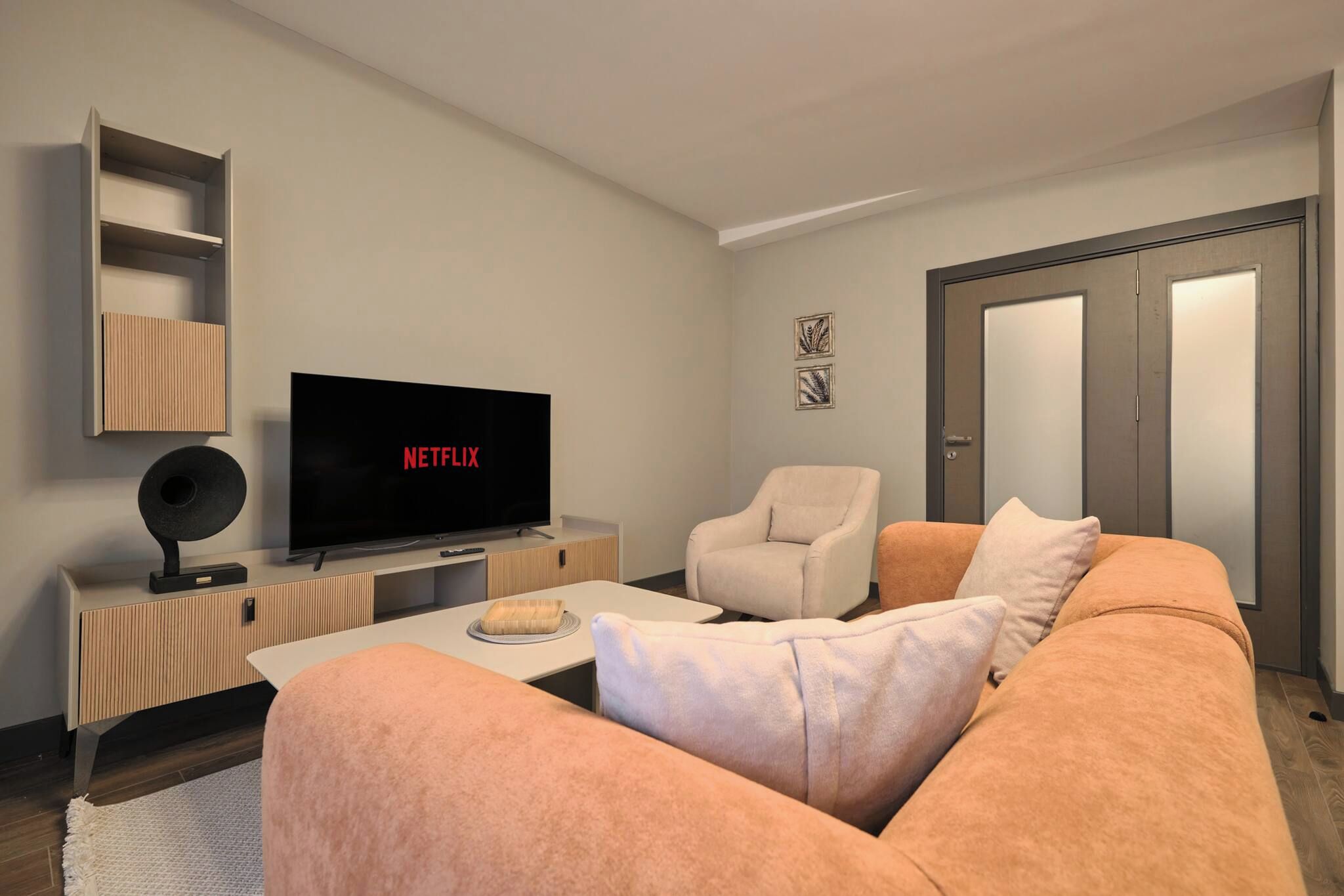En moderne stue med et fladskærms-tv, der viser Netflix, en sofa, en lænestol og et lille bord med en skål.